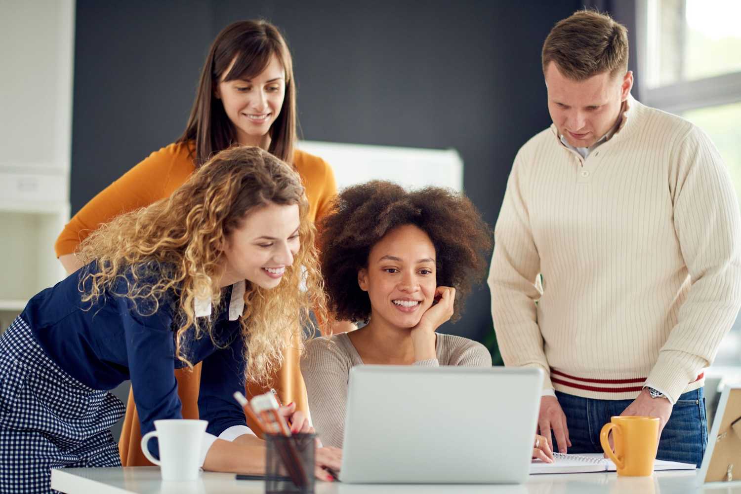 Happy group of coworkers standing around desk collaborating on medical bill review
