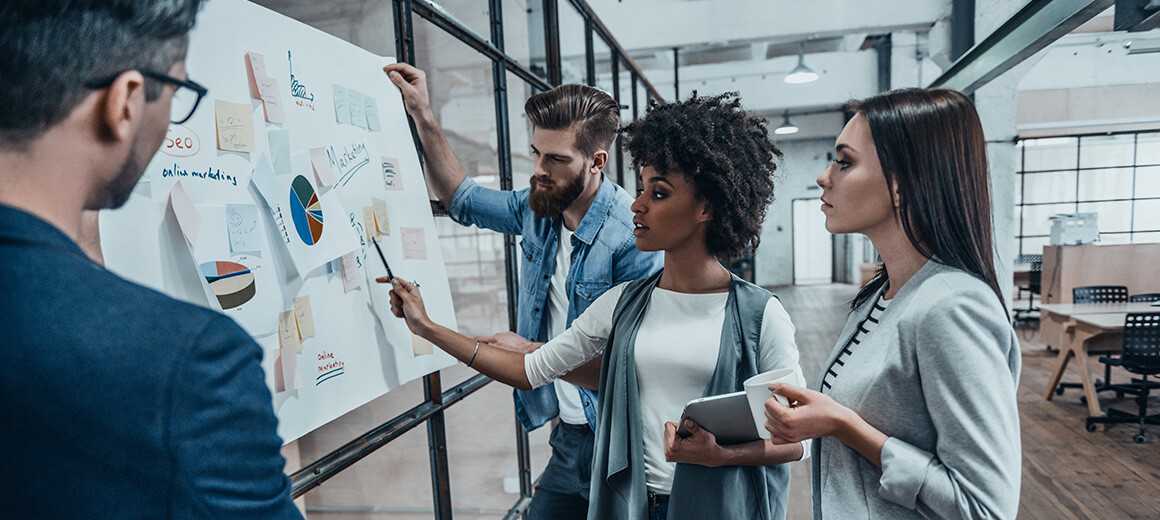 Four millennial colleagues looking at a board full of charts