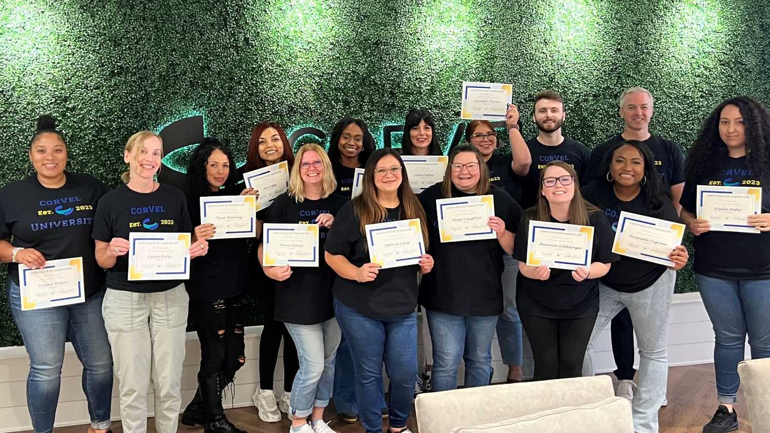 15 CorVel U Graduates, including Leslie Fallon, standing together with their certificates of completion at the CorVel Irvine office